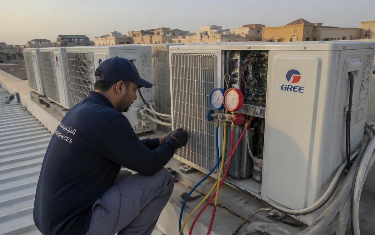 فني شركة الأمانة يفحص وحدات مكيفات خارجية متجاورة على سطح منزل في جنوب الرياض